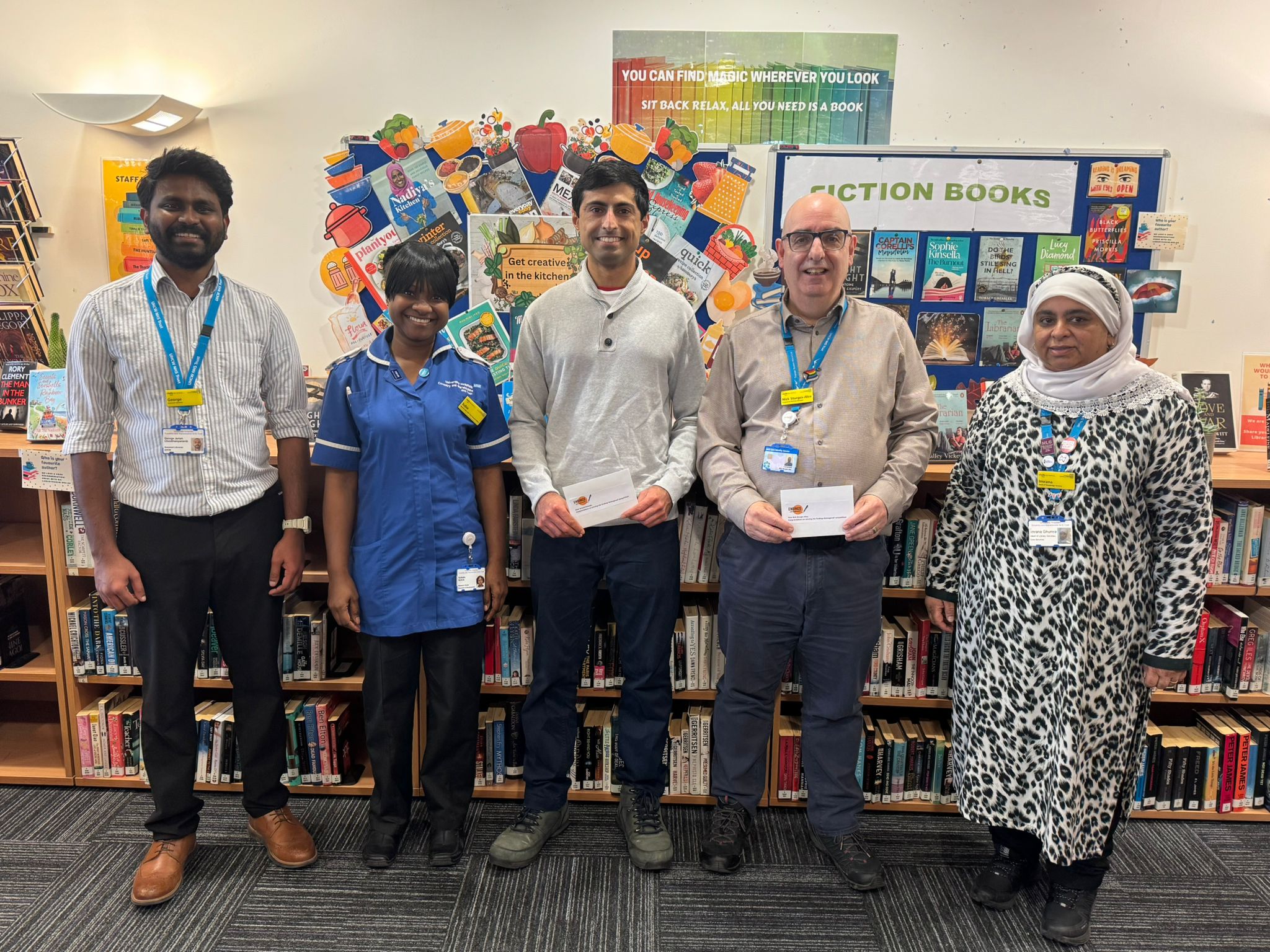 Image of staff in front of library bookshelves having been awarded prizes in a competition