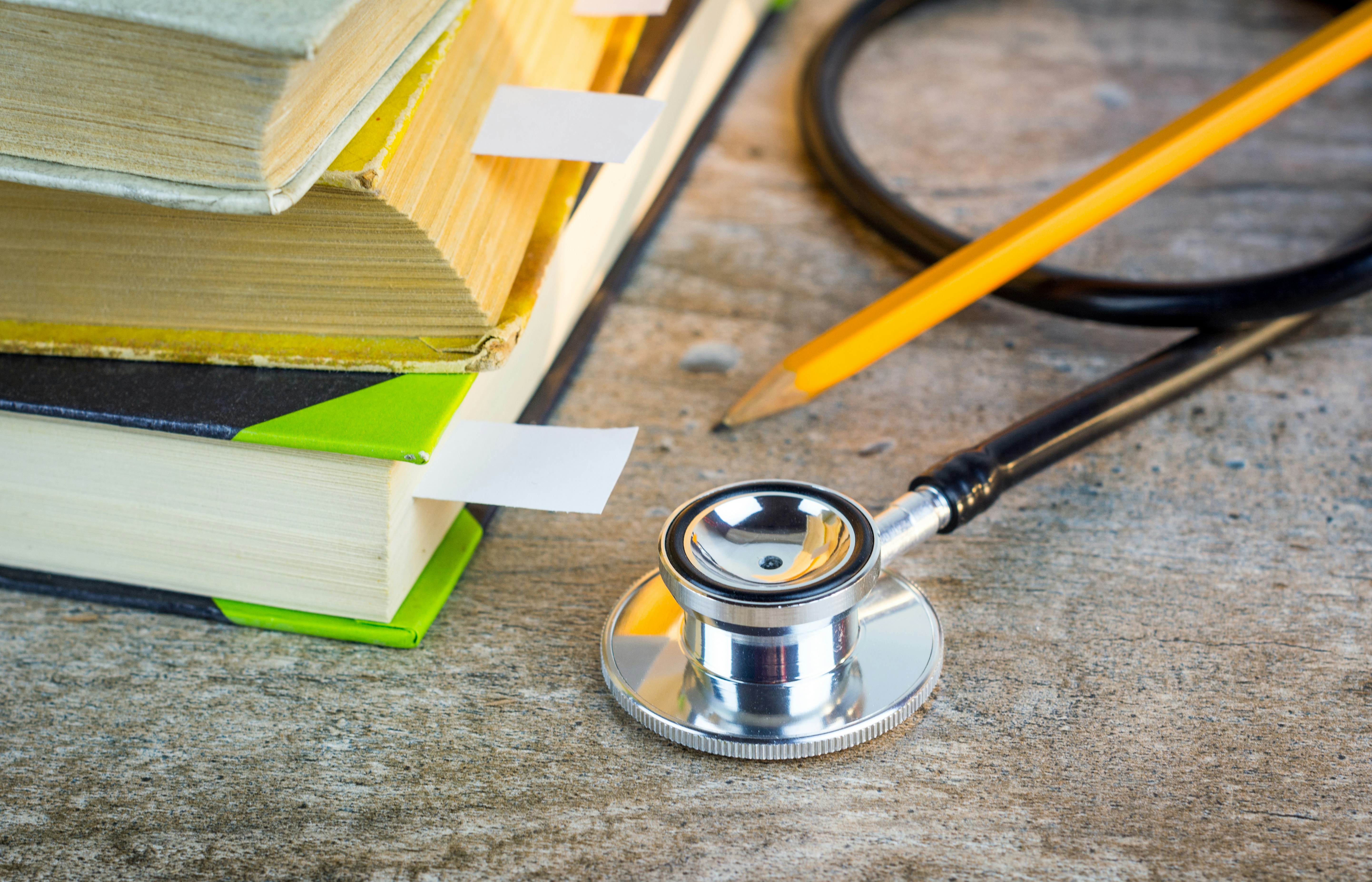 Stethoscope lying near a stack of textbooks with pages marked by colourful tabs.