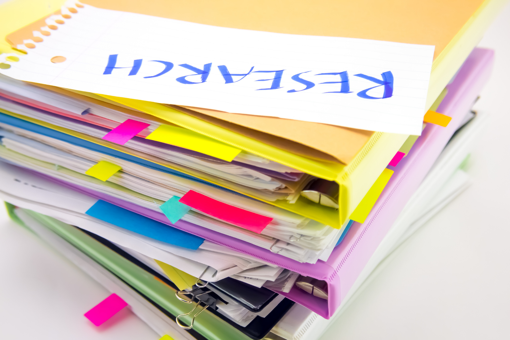 Stack of research materials, some of which have page markers in, indicating pages to be read
